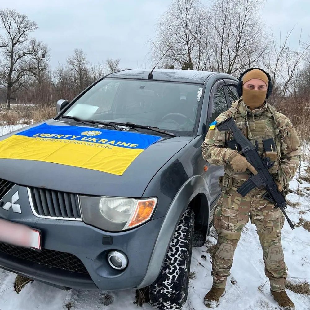 A defender beside an evacuation pickup draped in a Liberty Ukraine flag